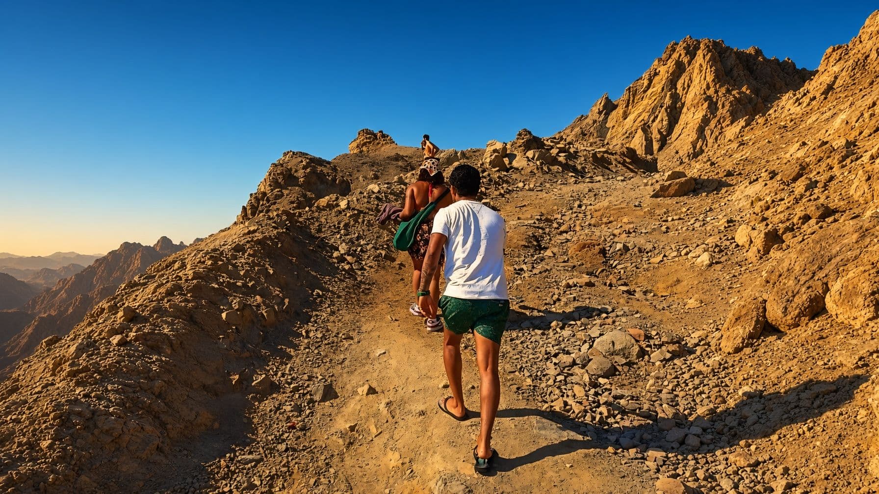 Hikers walking up a rocky mountain trail in the South Sinai sun