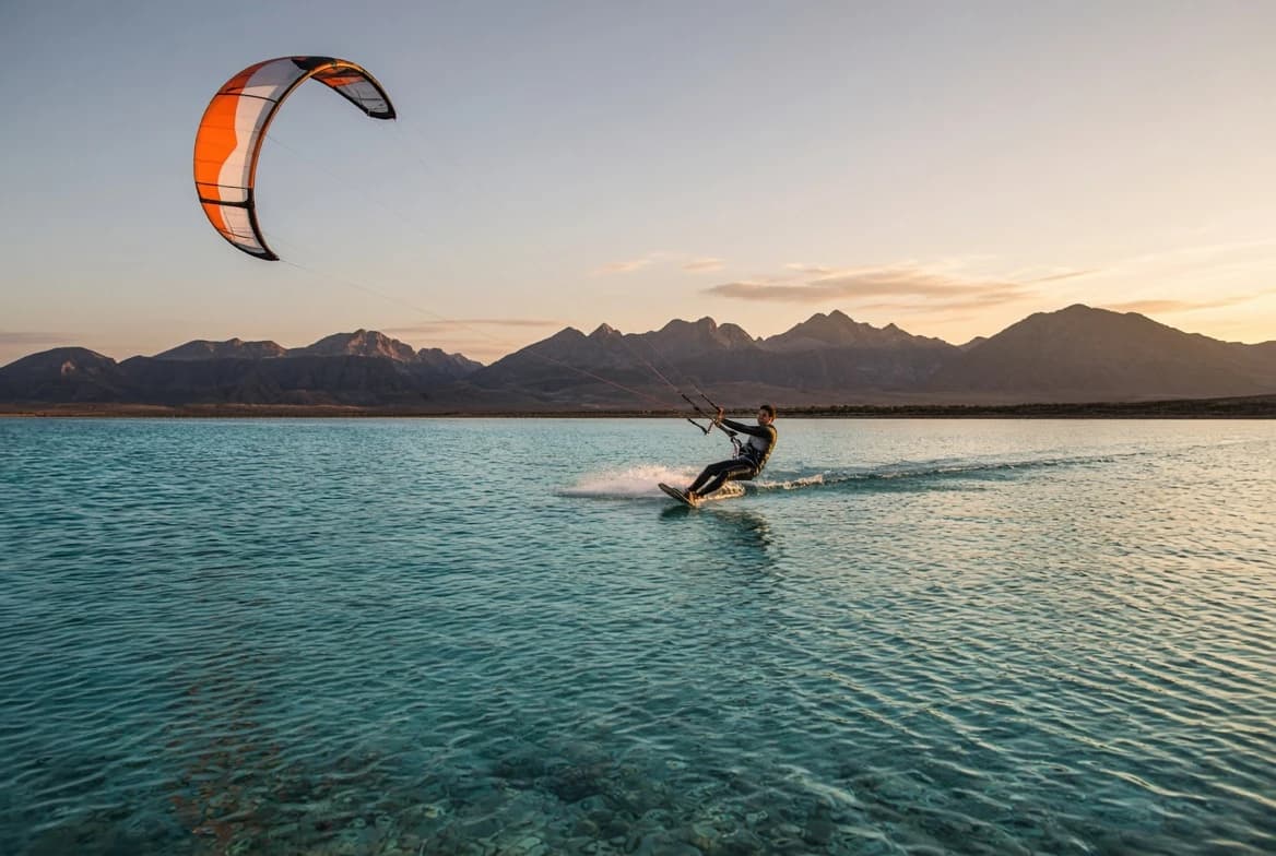 Kitesurfer riding turquoise water at sunset with an orange kite and the South Sinai mountains behind