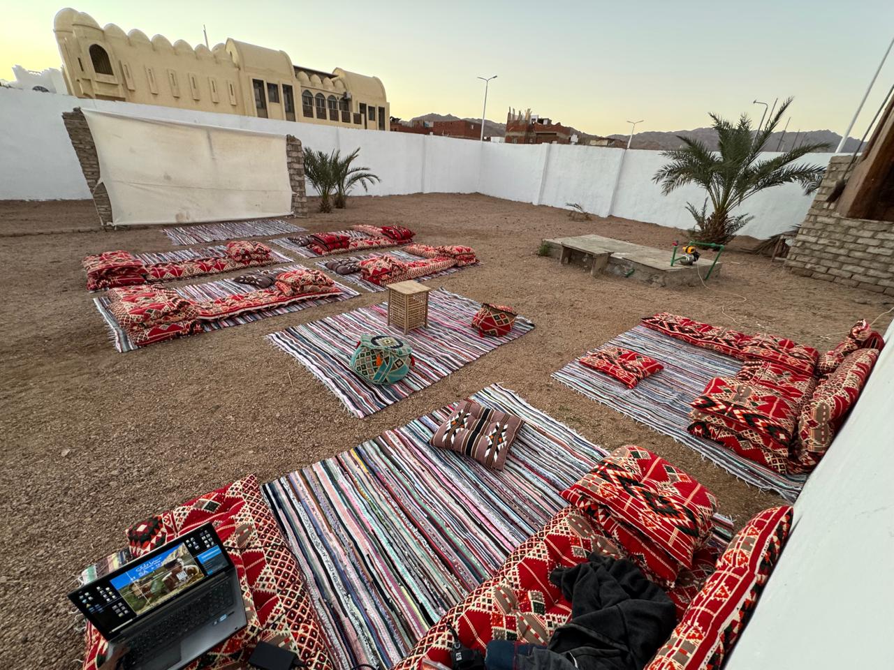 Open-air courtyard of SA Studios Dahab with Bedouin floor seating, palm trees and mountains behind
